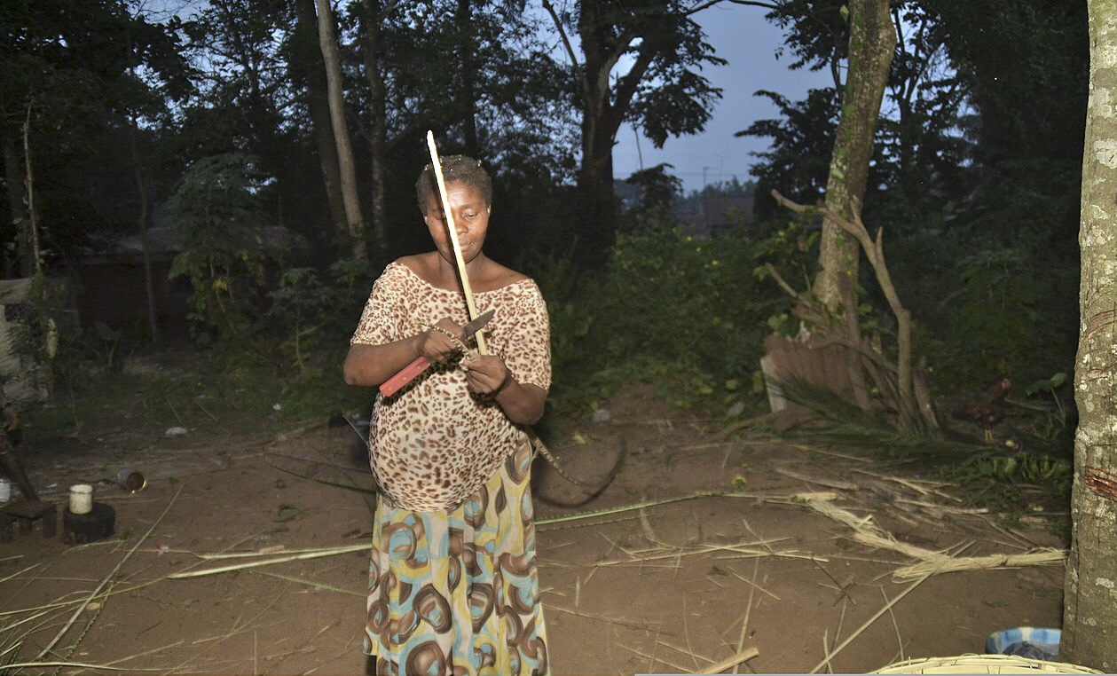 A woman preparing palm-frond materials for basket weaving in Nigeria.
